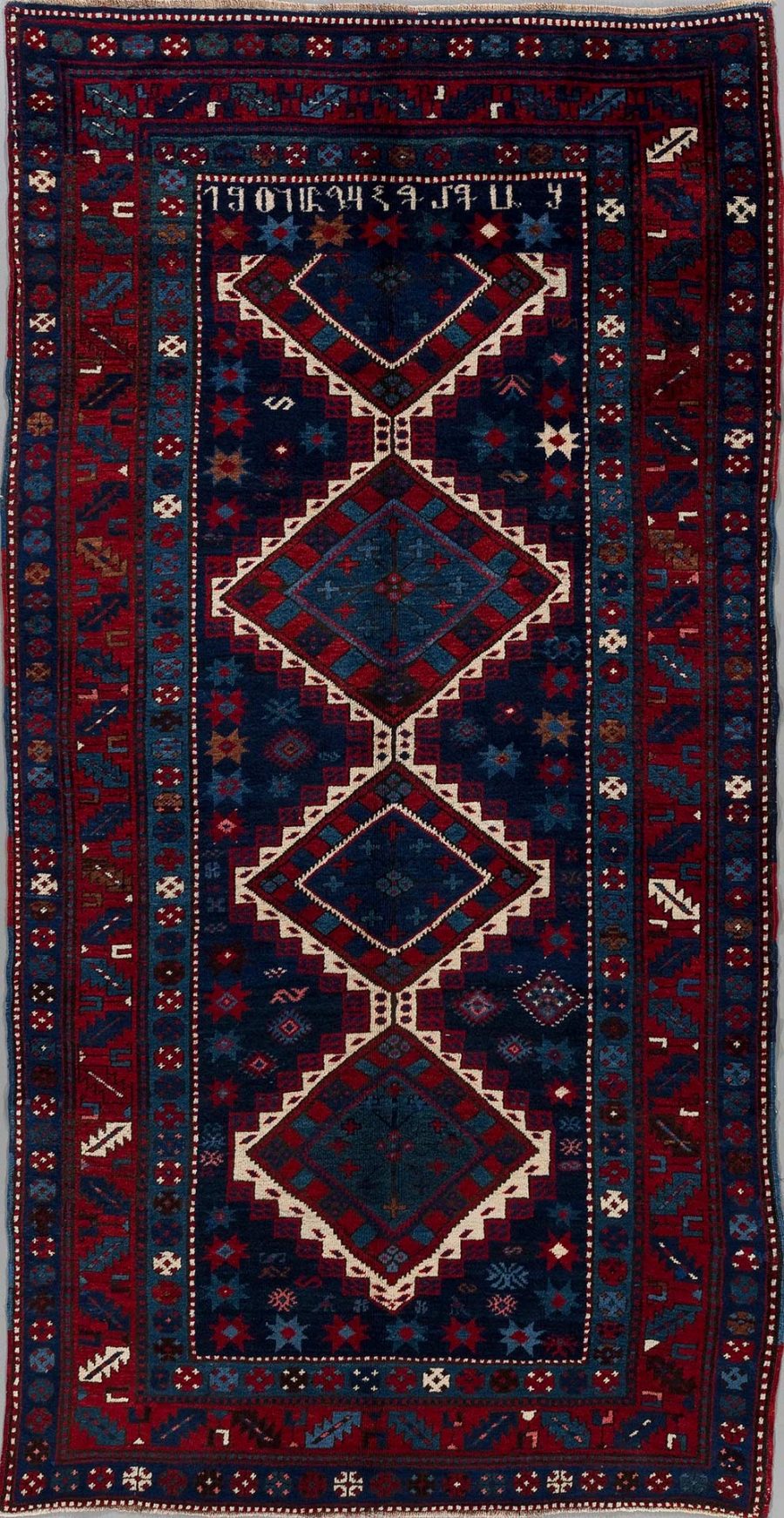 Traditioneller handgeknüpfter Teppich mit komplexem Muster in überwiegenden Farben von Blau und Rot, umrandet von Bordüren mit geometrischen und symbolartigen Motiven. Drei große verbundene Diamantformen zieren die Mitte, umgeben von kleineren dekorativen Elementen und Sternen.