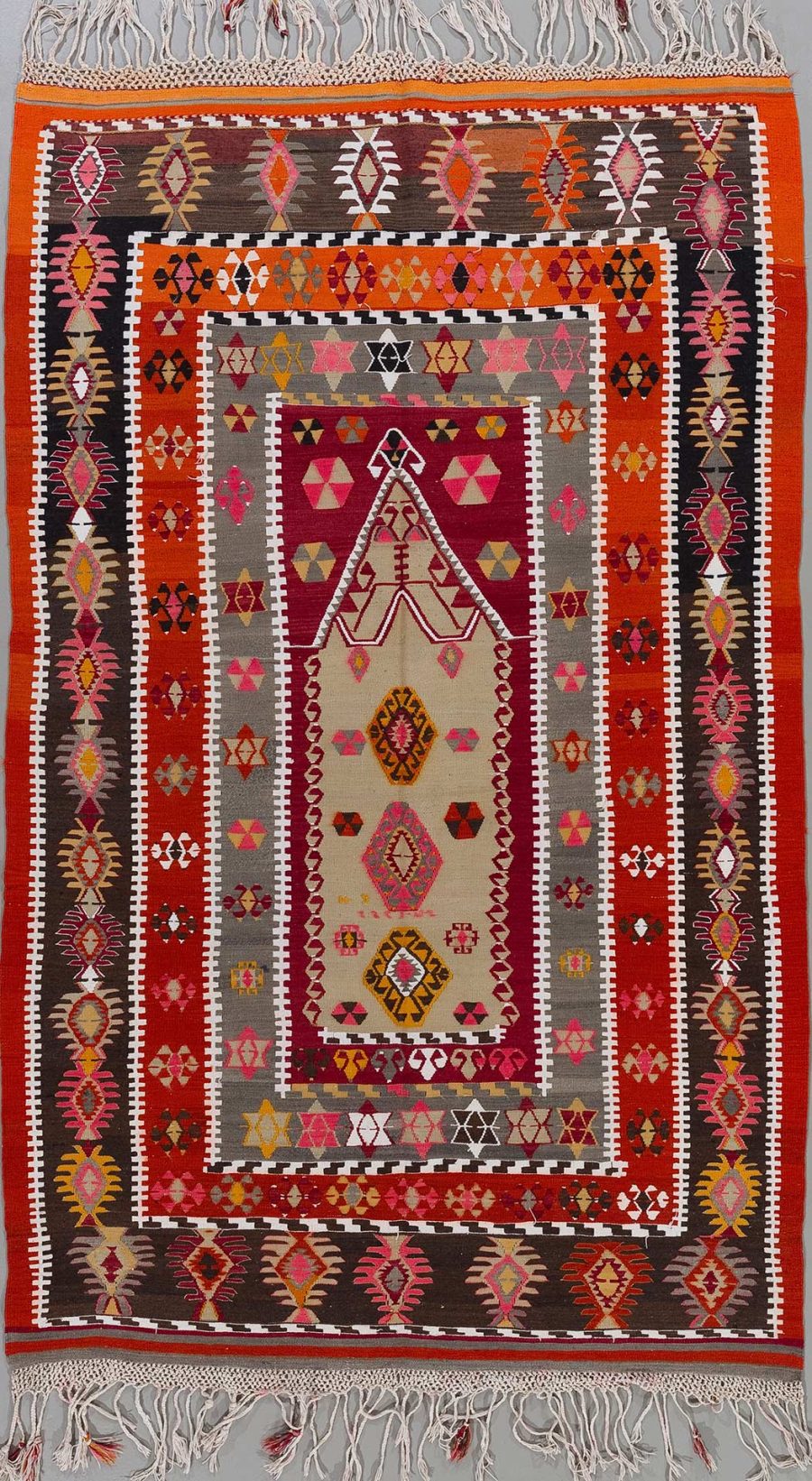 Handgewebter Teppich mit komplexem Muster in rot, braun, beige, schwarz und orange, mit zentralem Diamantmotiv und mehreren Bordüren in geometrischen Formen, abgeschlossen durch weiße Fransen an den Enden.