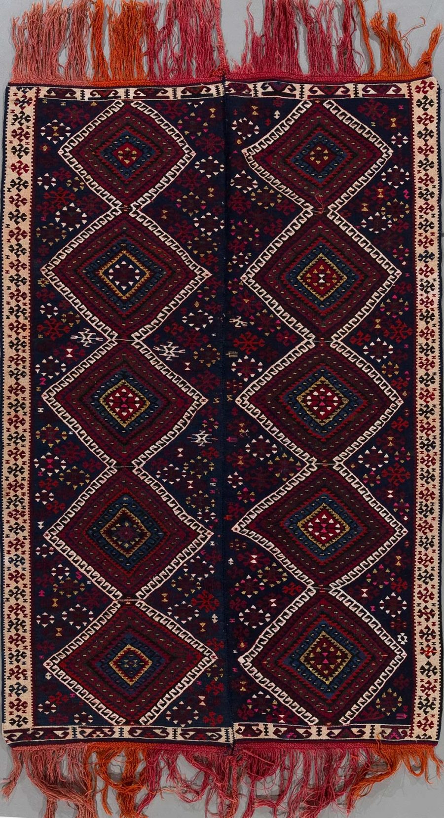 Traditioneller, handgewebter Teppich mit symmetrischen geometrischen Mustern in Rot-, Blau- und Beigetönen sowie Fransen an beiden Enden.