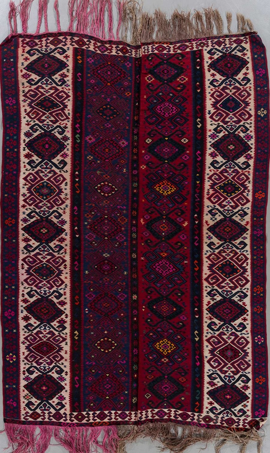 Traditioneller handgewebter Teppich mit komplexen Mustern in Dunkelrot, Blau und Beige, dekoriert mit geometrischen und diamantähnlichen Formen, versehen mit Fransen an beiden Enden.