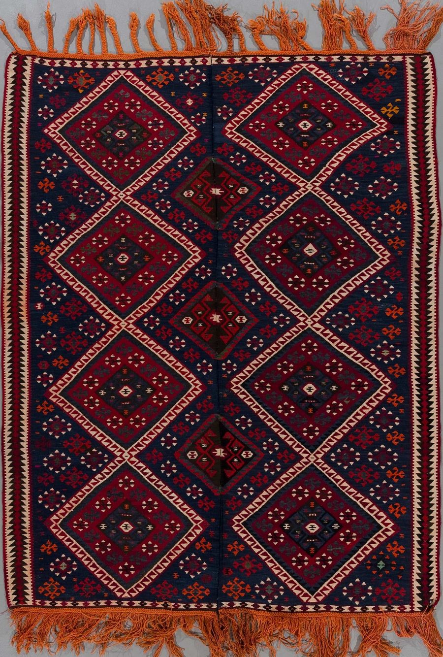 Traditioneller handgewebter Teppich mit geometrischen Mustern in Dunkelblau und Rot und orangefarbenen Fransen am unteren Ende.