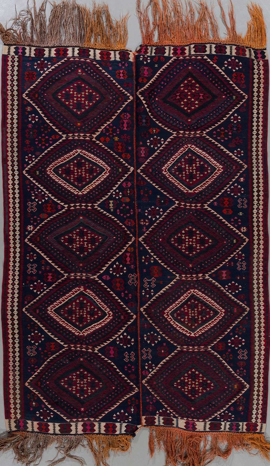 Traditioneller handgewebter Teppich mit symmetrischen geometrischen Mustern in Dunkelblau, Rot und Beige, mit Fransen an den Enden.