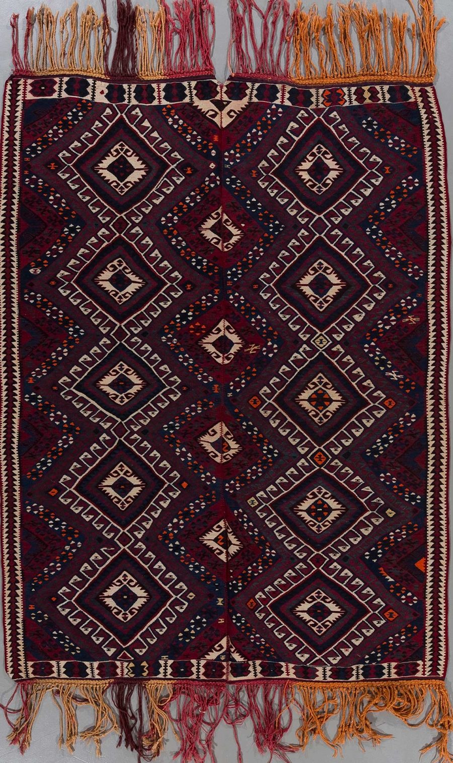 Traditioneller handgewebter Teppich mit komplexem Muster in Dunkelrot, Schwarz und Beige, dekoriert mit geometrischen Figuren und Fransen an den Enden.