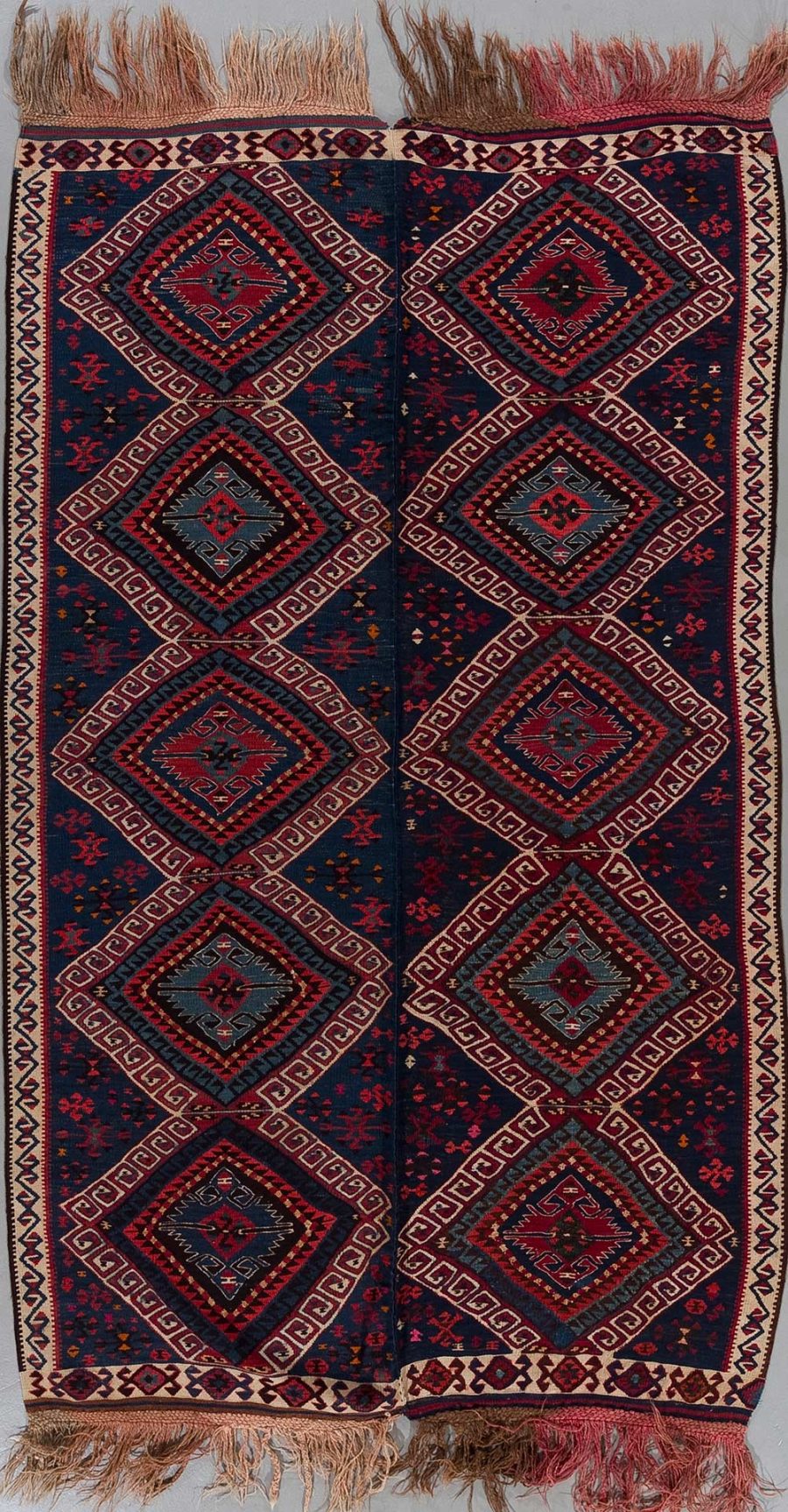 Handgeknüpfter, traditioneller Teppich in vertikaler Ausrichtung mit symmetrischem, geometrischem Muster in dunkelblauen, roten und beige Farbtönen, umgeben von Bordüren und mit Fransen an den Enden.