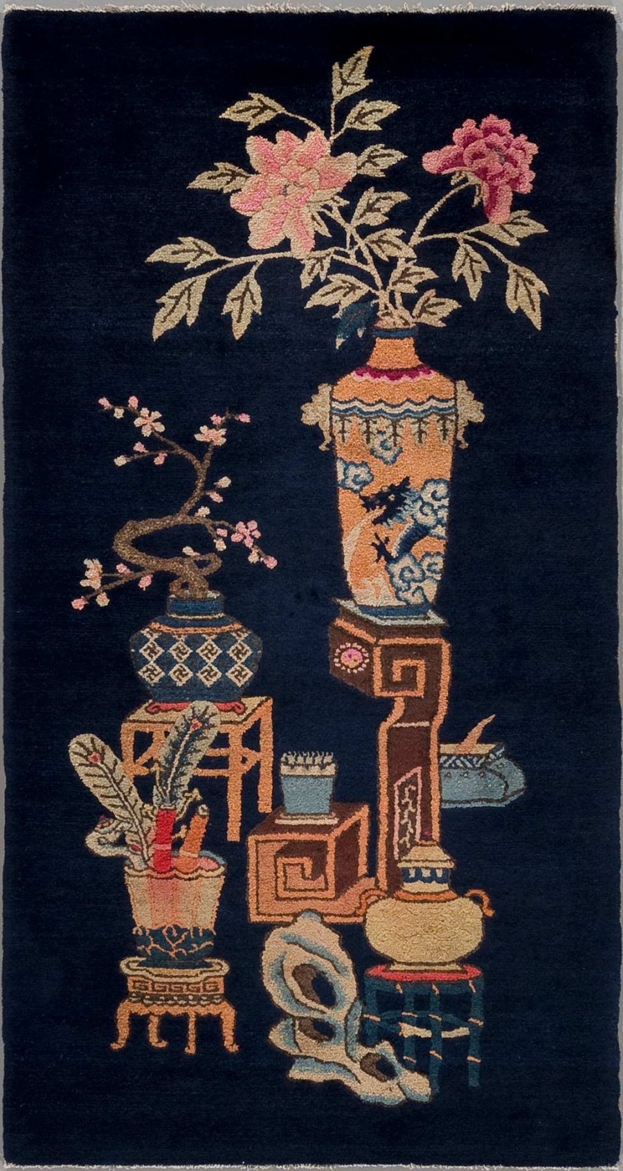 Antike asiatische Vasen und dekorative Objekte aufgestickt auf einem dunkelblauen Teppich mit floralen Motiven und Mustern.