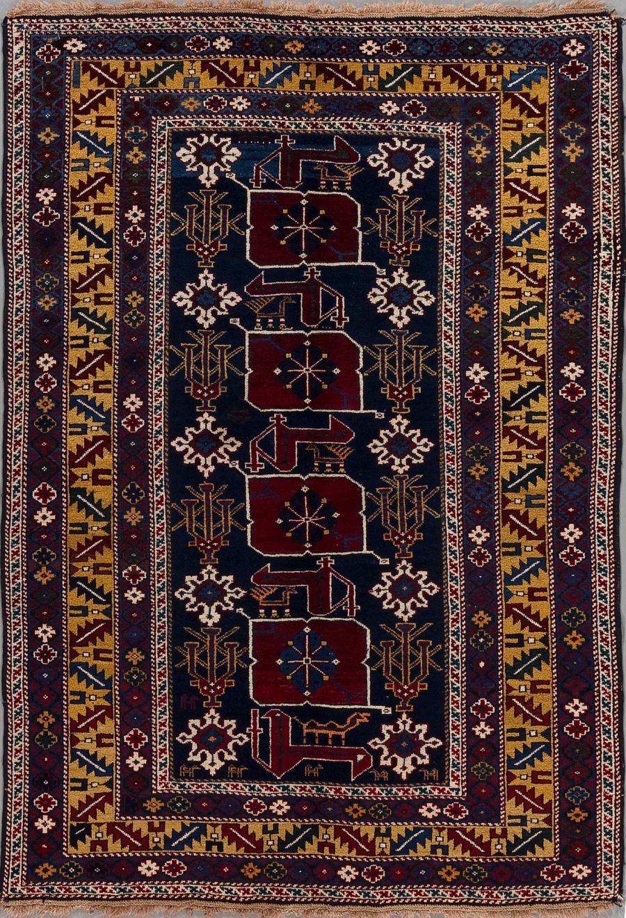 Detailliert gewebter orientalischer Teppich mit einem zentralen, dunkelblauen Feld und mehreren geometrischen, pflanzlichen und tierischen Motiven in Rot, Weiß, Blau und Goldtönen. Die Umrandung des Teppichs besteht aus mehreren schmalen Bordüren mit aufwändigen Mustern in ähnlichen Farbkombinationen.
