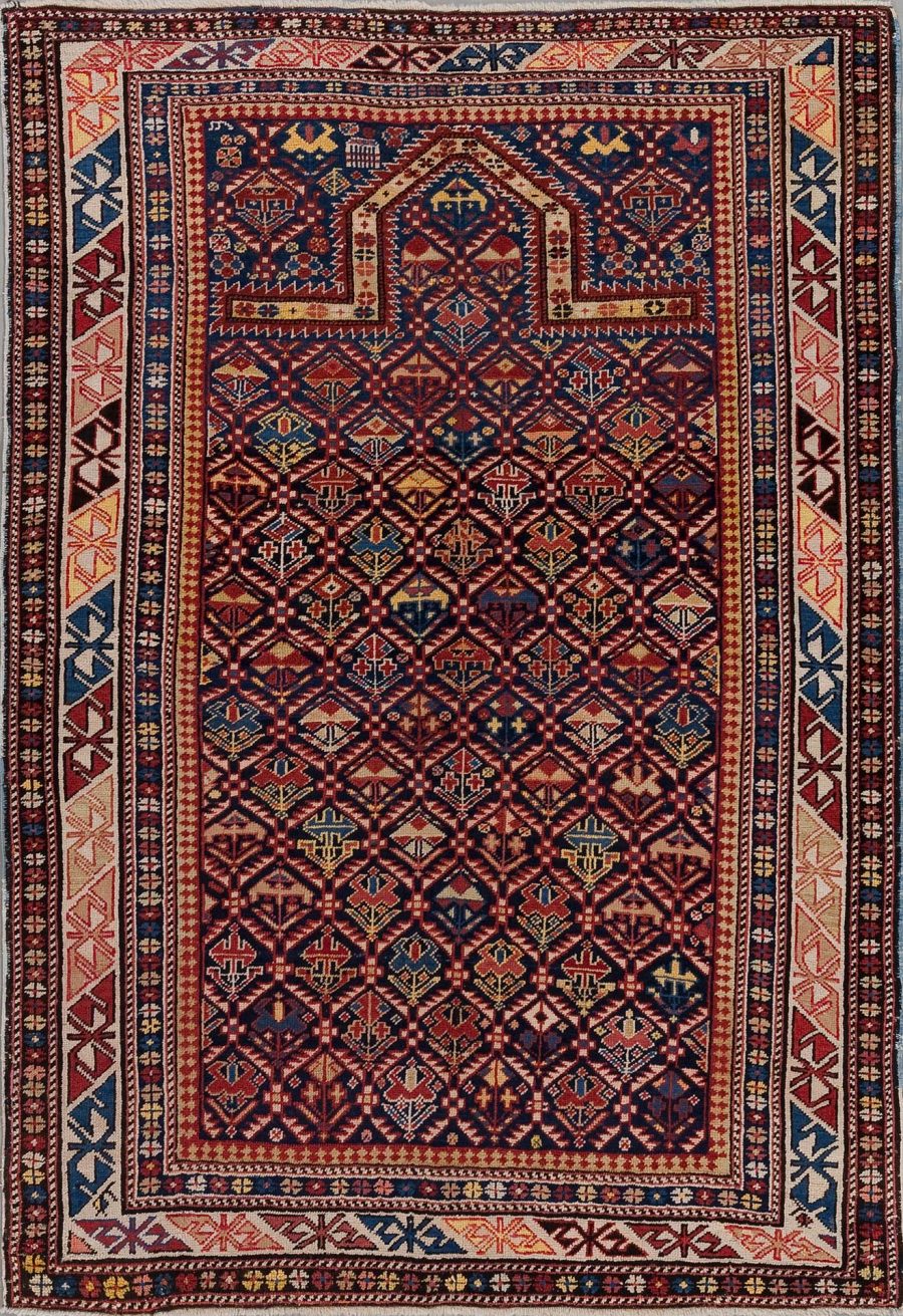 Traditioneller handgeknüpfter Teppich mit komplexem geometrischen Muster und mehreren Bordüren in Rottönen, Marineblau, Beige und Akzenten in Gelb-Grüntönen.