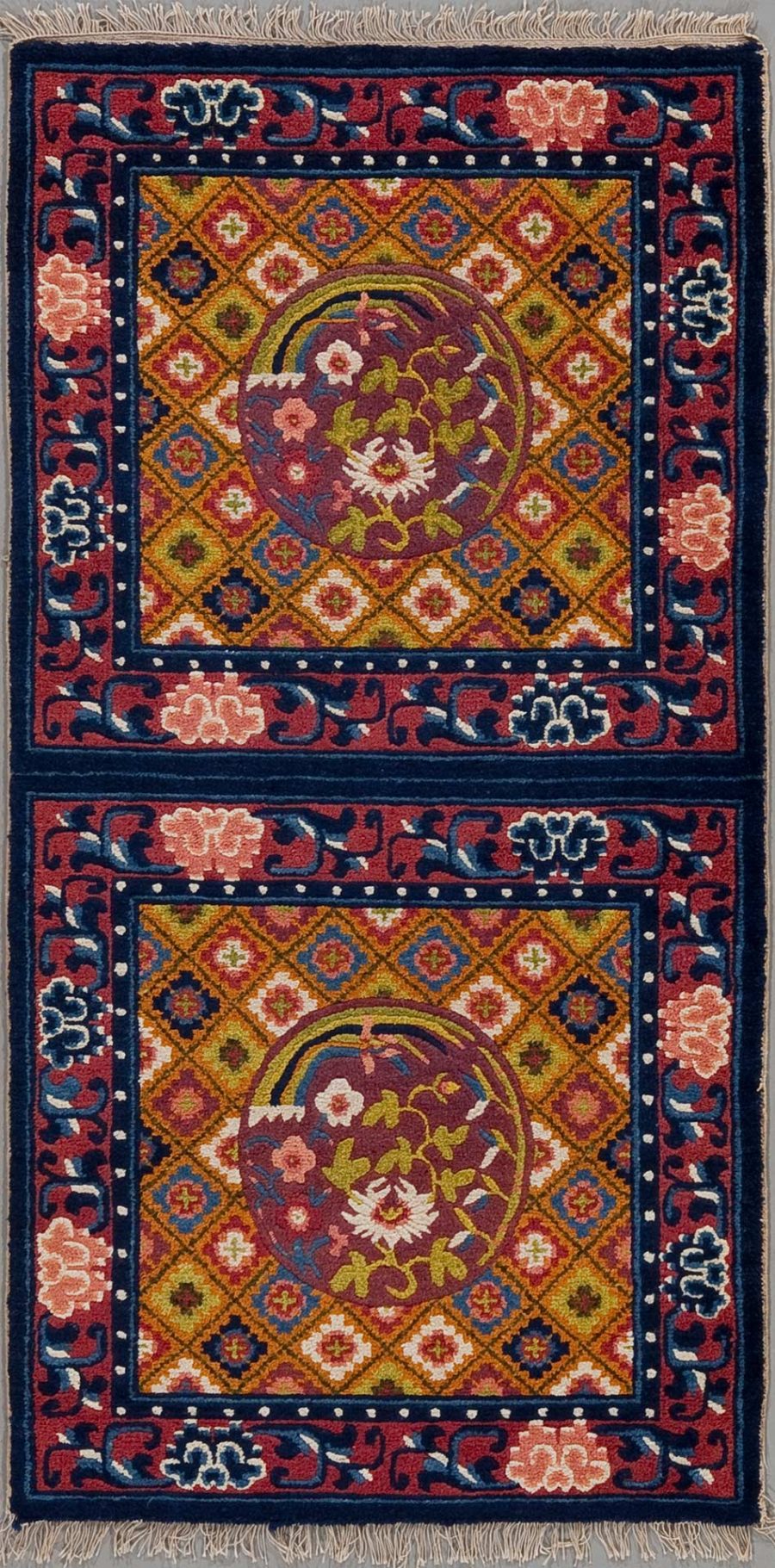 Traditioneller handgeknüpfter Teppich mit zwei zentralen Medaillons auf burgunderrotem Grund, umgeben von geometrischen und floralen Mustern in Blau, Orange und Creme, mit einer dunkelblauen Bordüre und Fransen an den Enden.