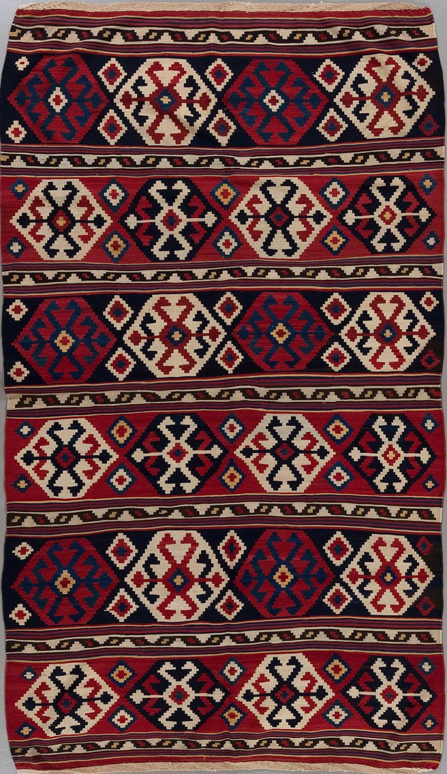 Traditioneller handgewebter Teppich mit wiederholenden geometrischen Mustern und Medaillons in Rot, Blau, Beige und Schwarz.