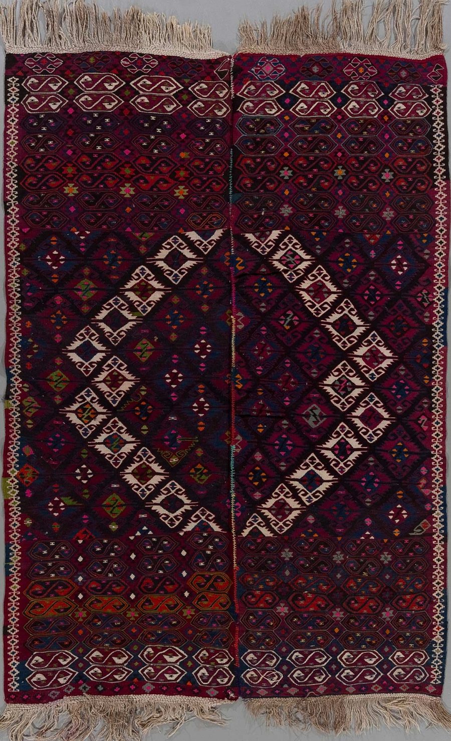 Traditioneller, handgewebter Teppich mit komplexem, geometrischem Muster in vorwiegend dunklen Burgunder-, Blau- und Beigetönen und Fransen an den Enden.
