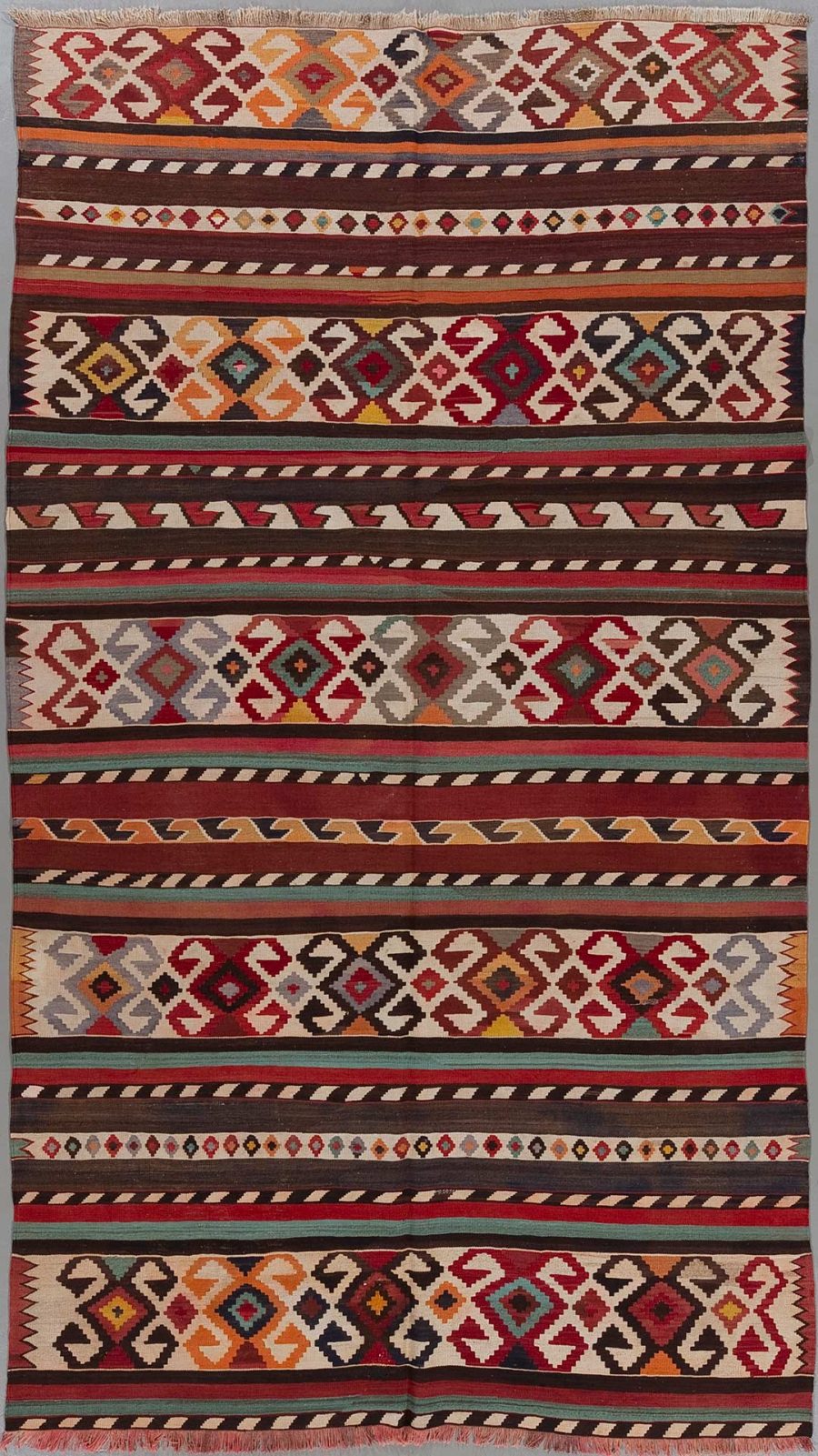 Vertikal ausgerichteter, handgewebter Teppich mit traditionellen ethnischen Mustern in einer Vielfalt an Farben, darunter Rot, Braun, Orange, Weiß und Schwarz, angeordnet in wiederkehrenden geometrischen Formen und Streifen.