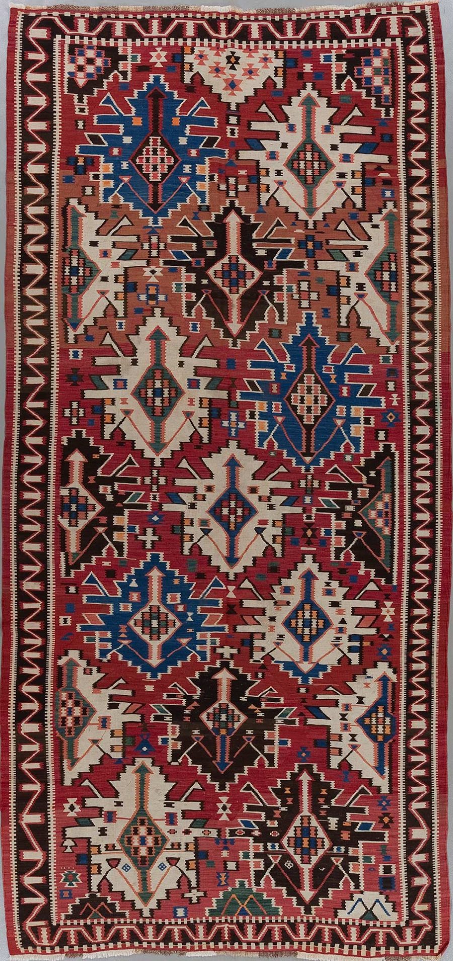 Traditioneller handgewebter Teppich mit komplexen geometrischen Mustern und symbolischen Designs in Rot-, Blau-, Braun- und Cremetönen, mit ausgeprägten Bordüren und fransenlosen Enden.