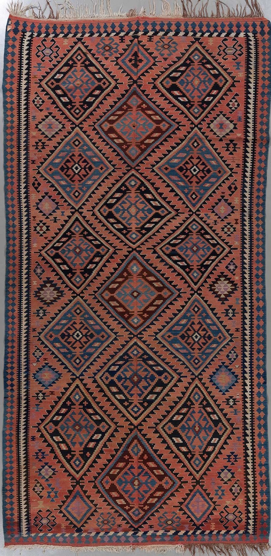 Traditioneller handgewebter Teppich mit komplexem Muster aus Diamanten und geometrischen Formen in Erdtönen mit blauen und roten Akzenten.