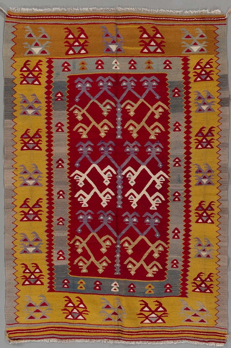 Handgewebter Teppich mit traditionellen geometrischen Mustern in Rot, Gelb, Weiß und Grau sowie Fransen an den Enden.
