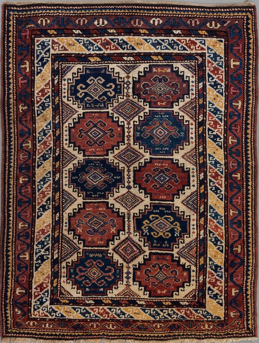 Traditioneller handgeknüpfter Teppich mit komplexen geometrischen Mustern und Bordüren in Rottönen, Blau, Beige und Akzenten von Weiß, aufgenommen aus der Vogelperspektive.