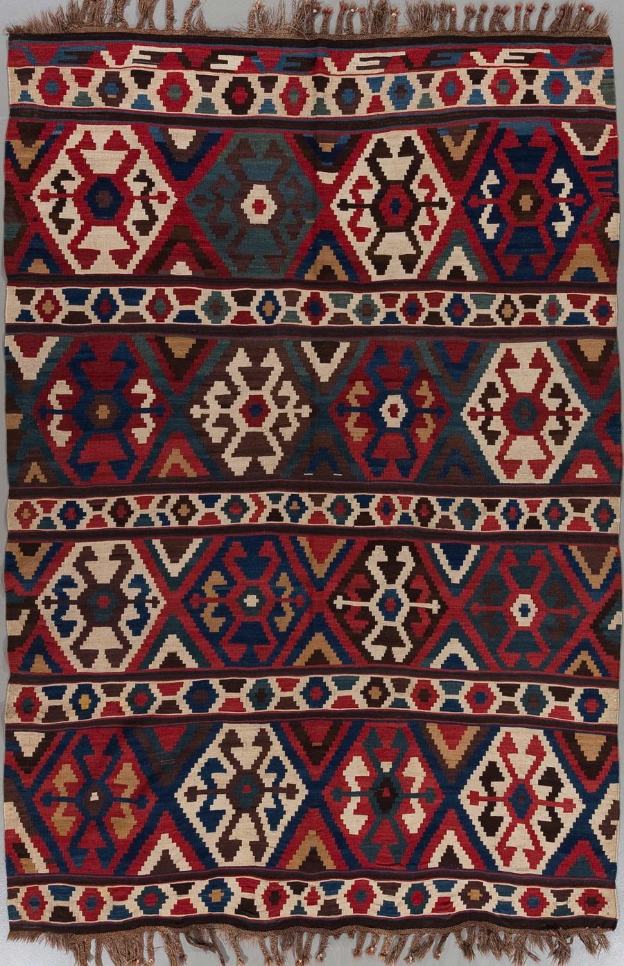 Traditioneller handgeknüpfter Teppich mit komplexem Muster in Rot-, Blau-, Beige- und Brauntönen mit dekorativen Fransen an den Enden.