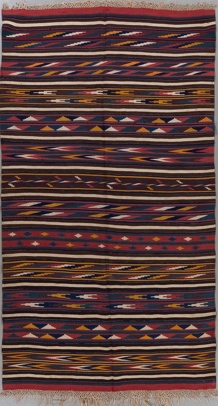 Handgewebter Teppich mit traditionellen ethnischen Mustern in verschiedenen Farben wie Rot, Dunkelblau, Gelb und Weiß, aufgehängt und vollständig sichtbar mit Fransen an beiden Enden.