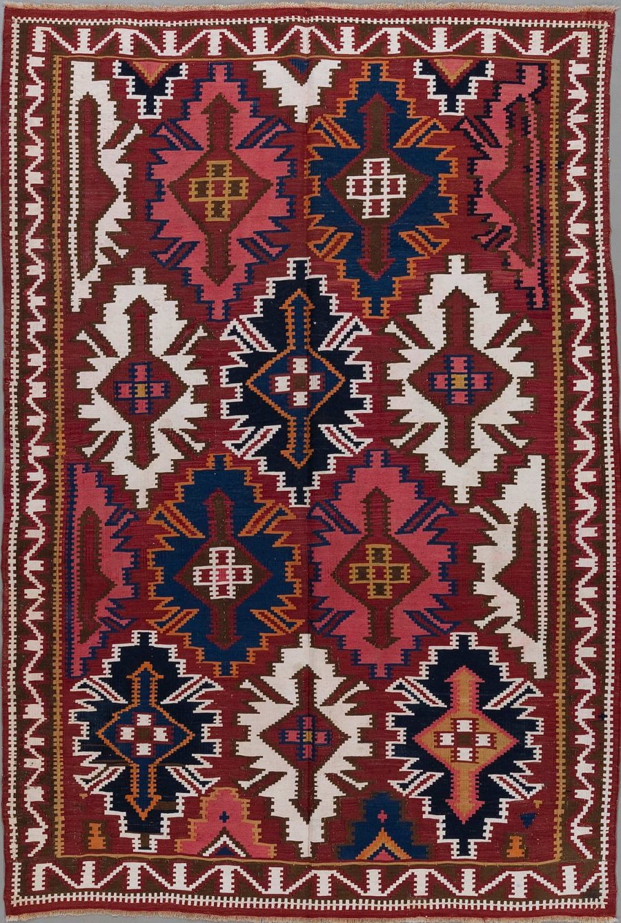 Traditioneller handgewebter Teppich mit komplexem geometrischem Muster in Farben wie Dunkelrot, Blau, Beige und Weiß. Er zeigt symmetrische Anordnungen von Medaillons, Sternen und Zickzacklinien, die von einer Grenze mit ähnlichen Motiven umrahmt sind.