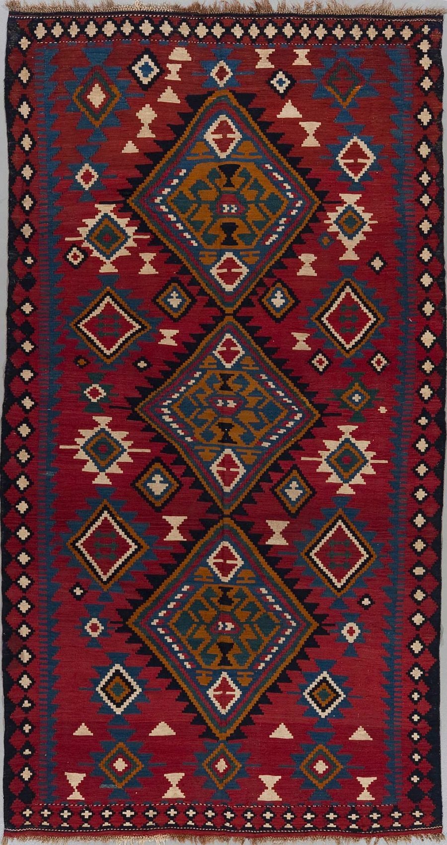 Traditioneller handgewebter Teppich mit ineinandergreifenden geometrischen Mustern in Rot-, Blau- und Beigetönen mit drei großen zentralen Diamantfiguren und aufwendigen Rahmenmotiven.