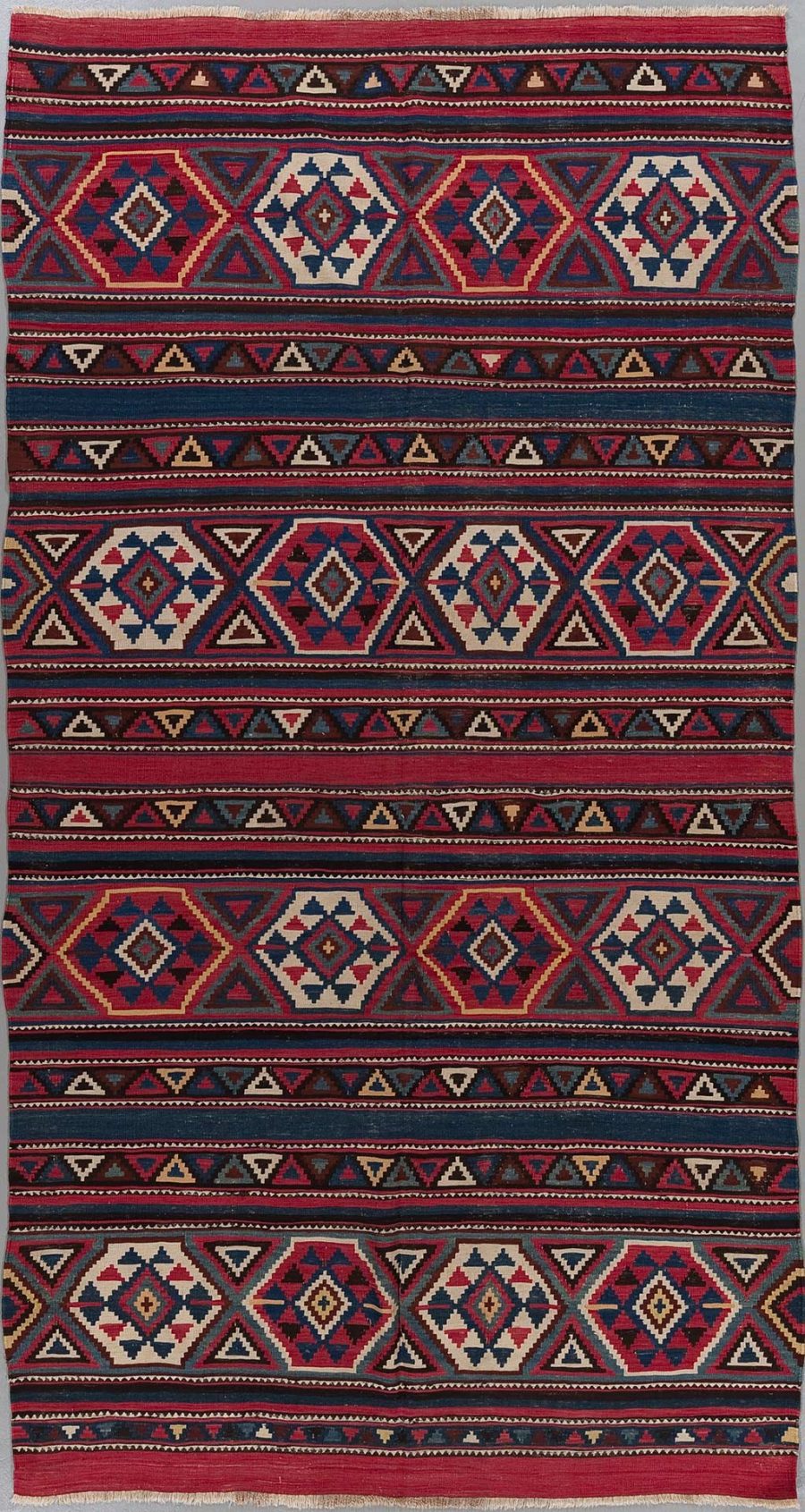 Traditioneller handgewebter Teppich mit wiederholten Mustern in Rot, Blau, Weiß und Beige.