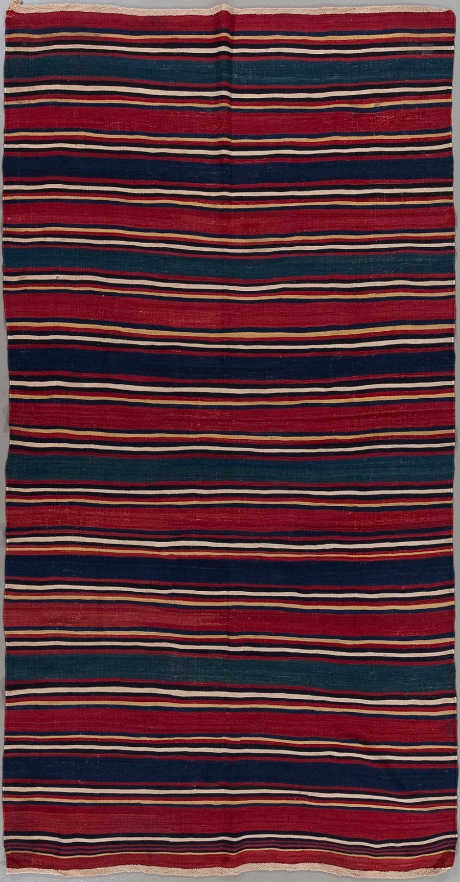 Traditioneller handgewebter Teppich mit horizontalen Streifen in abwechselnden Farben von Rot, Dunkelblau und gelblichen Akzenten auf einem groben, ungebleichten Stoff.