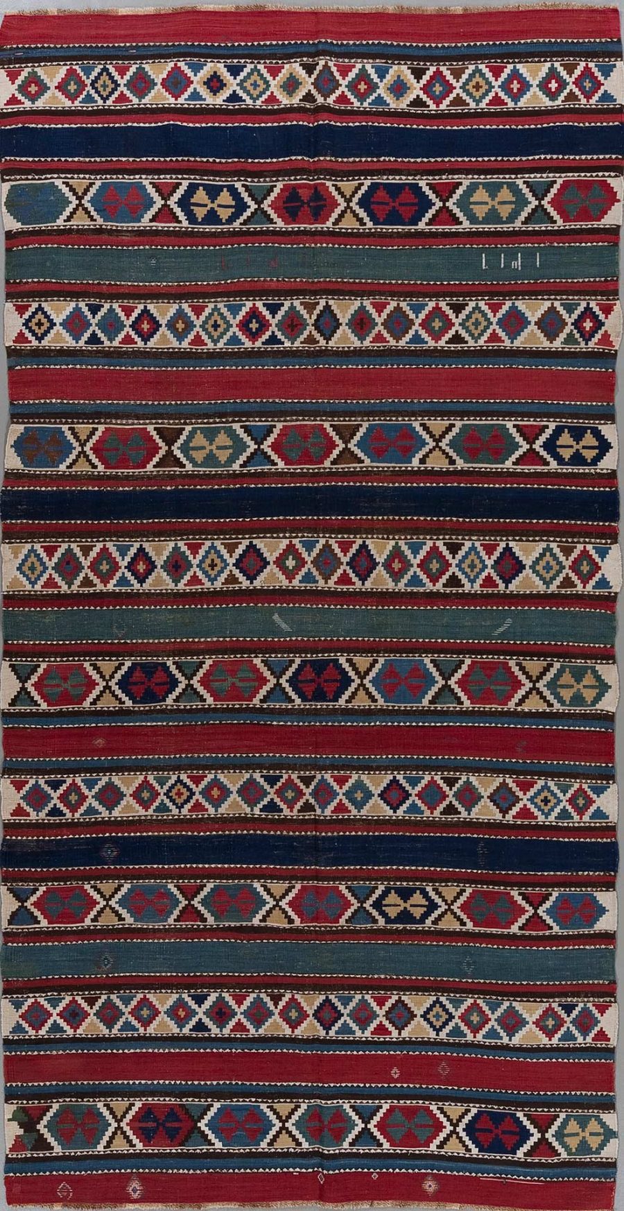 Traditioneller handgewebter Teppich mit mehrfarbigen, geometrischen Mustern und Streifen in Rot, Blau, Beige und anderen Farben.