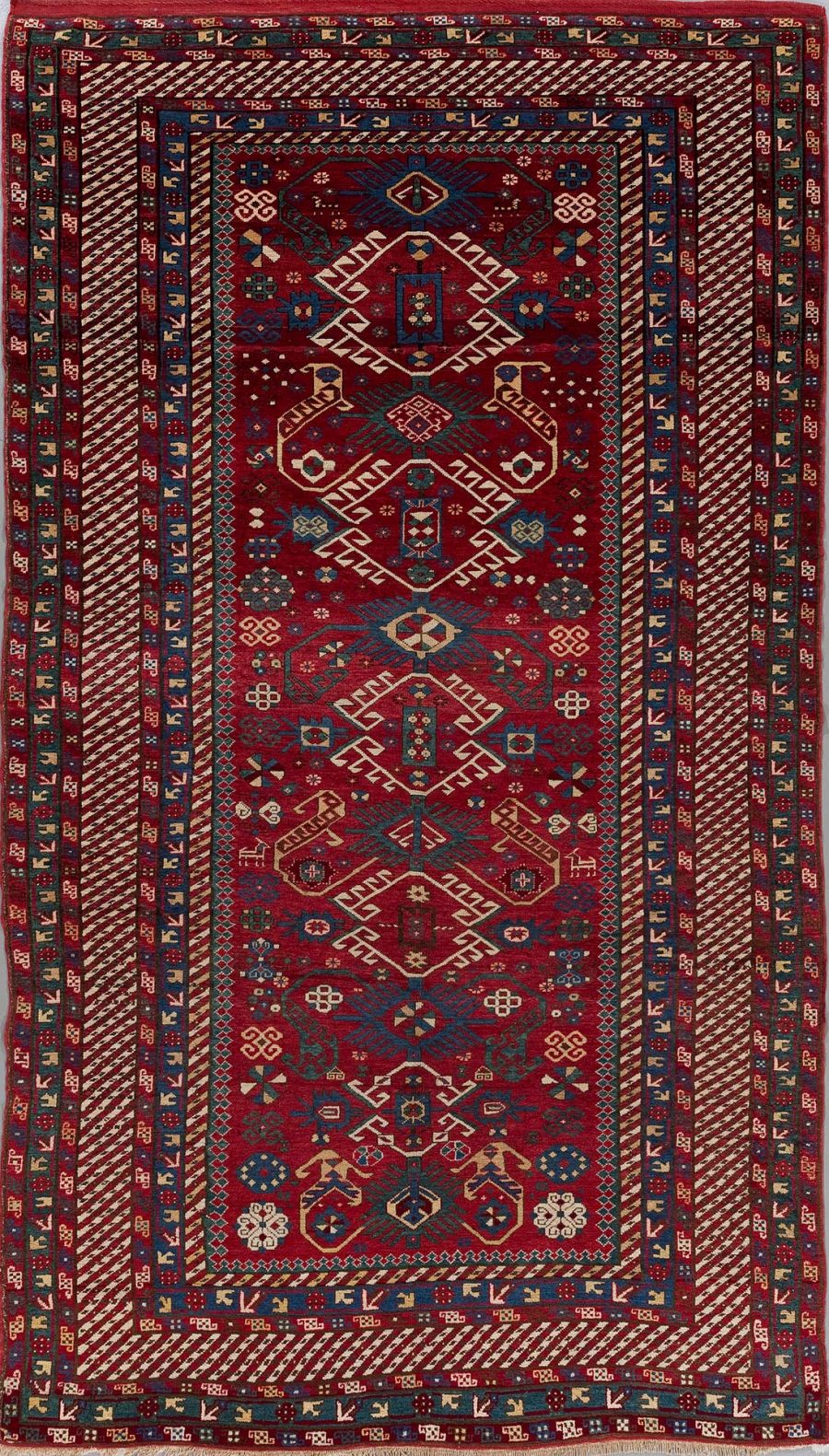 Traditioneller, handgewebter Teppich mit komplexen Mustern in Rot-, Blau- und Beigetönen, mit zentralen geometrischen und floralen Designelementen, umgeben von mehreren bestickten Bordüren.