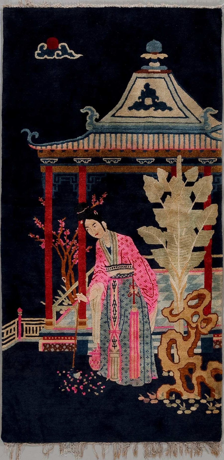 Antikes handgeknüpftes Wandteppich mit einer Darstellung eines traditionell gekleideten asiatischen Mädchens neben einer Pagode und blühenden Pflanzen, auf dunklem Hintergrund mit stilisierter Sonne und Wolken oben im Bild.