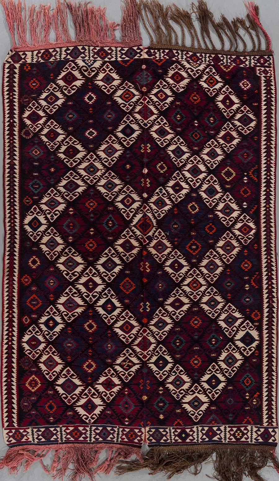 Traditioneller handgewebter Teppich mit komplexem geometrischem Muster in Dunkelrot, Schwarz, Beige und Blautönen, umrandet von einem dekorativen Bordürenmuster und versehen mit Fransen an beiden Enden.