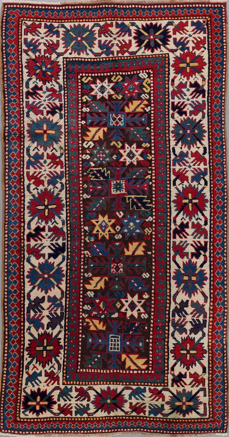 Traditioneller handgeknüpfter Teppich mit komplexem, geometrischem Muster in Rot-, Blau-, Weiß- und Gelbtönen mit mehrschichtigen Bordüren und einem zentralen dunklen Feld, das von einer breiten helleren Rahmenbordüre umgeben ist.