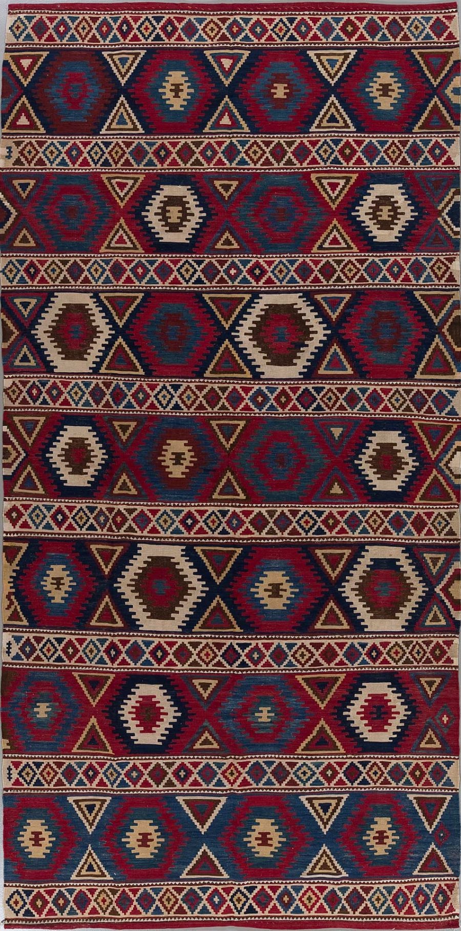 Traditioneller handgewebter Teppich mit wiederholenden geometrischen Mustern und Symmetrien in Rot-, Blau-, Beige- und Brauntönen.