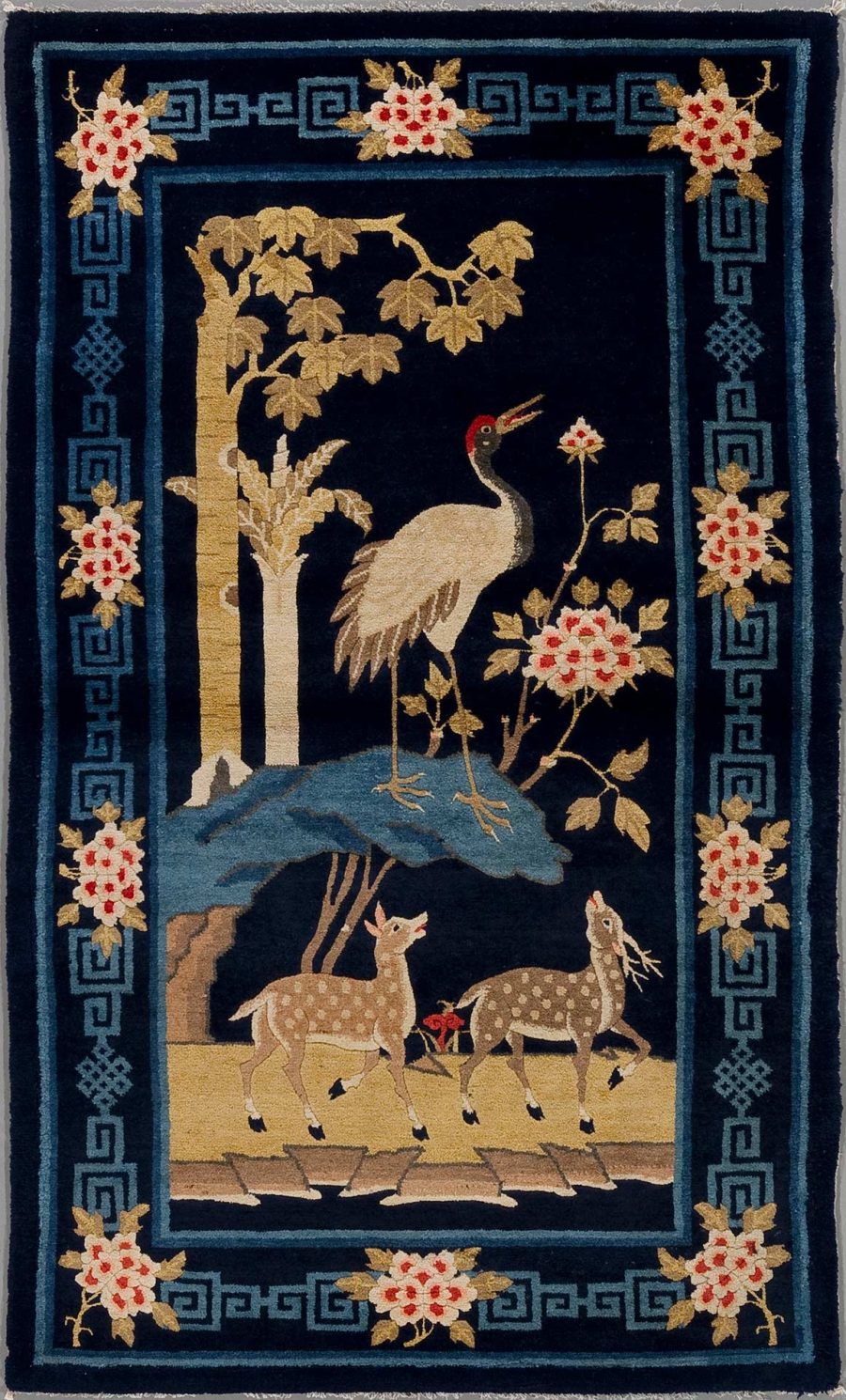 Ein detailliertes, handgearbeitetes Wandteppich mit asiatischen Motiven auf schwarzem Grund, darstellend einen großen Kranich neben einem Teich unter blühenden Bäumen und zwei Rehe auf einer Wiese, umrahmt von einem dekorativen Muster mit griechischem Schlüssel und floralem Design in den Farben Gold, Rot und Blau.