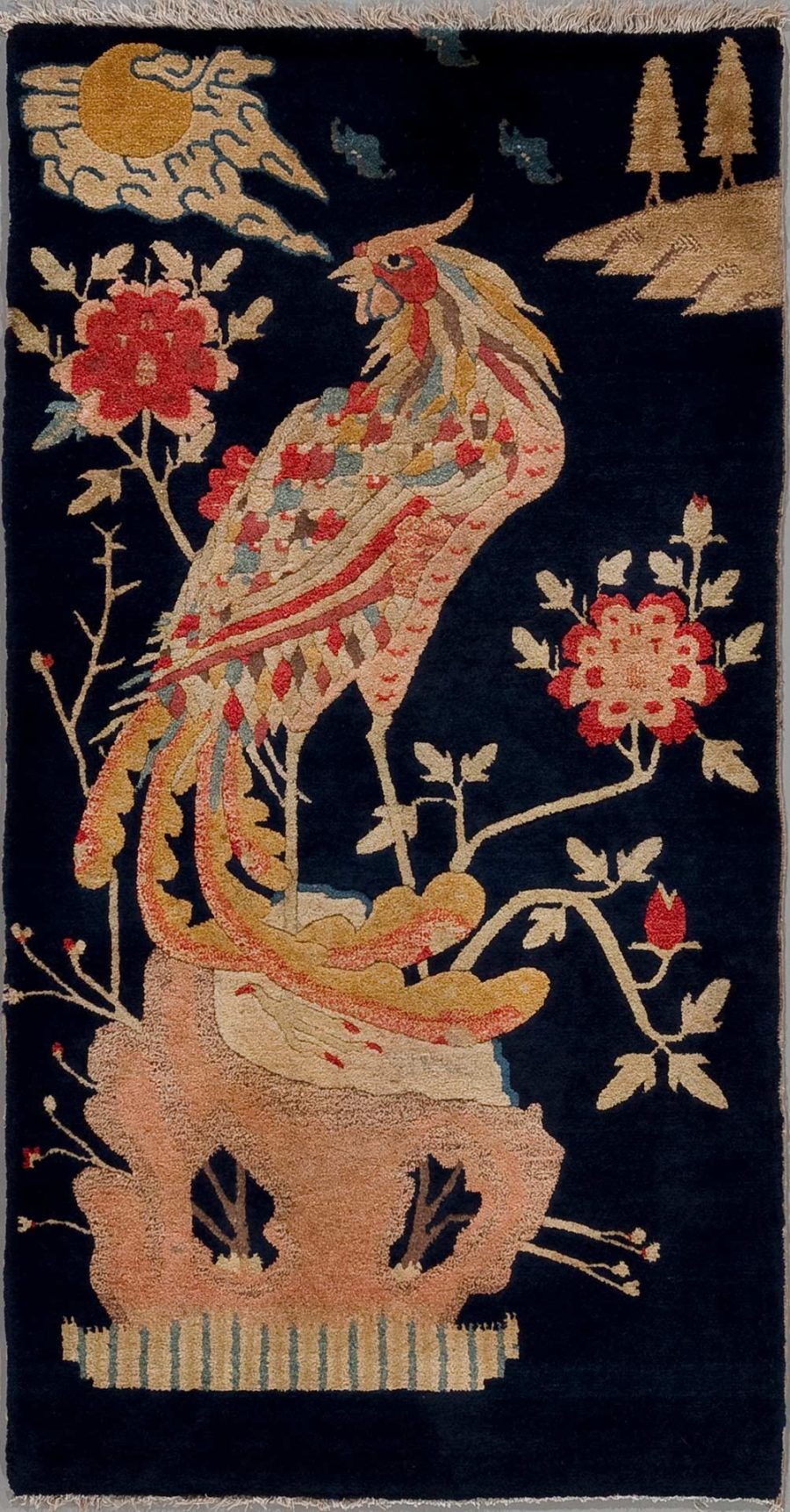 Alt-Text: Antiker Wandteppich mit der Darstellung eines farbenprächtigen Pfauens auf einem Blumentopf, umgeben von blühenden Pflanzen und Blumen gegen einen nachtblauen Himmel, mit einer stilisierten Sonne und Wolken im Hintergrund.