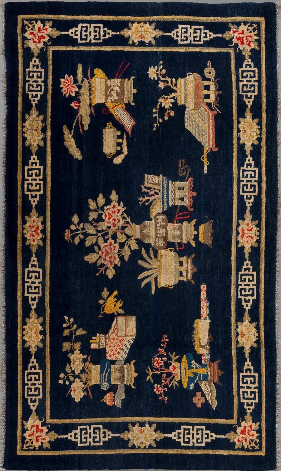 Antiker Teppich mit dunkelblauem Grund und orientalischem Dekor, umfasst florale Elemente und stilisierte Instrumente, umrandet von einem cremefarbenen und rot akzentuierten Griechisch-Schlüssel-Muster.