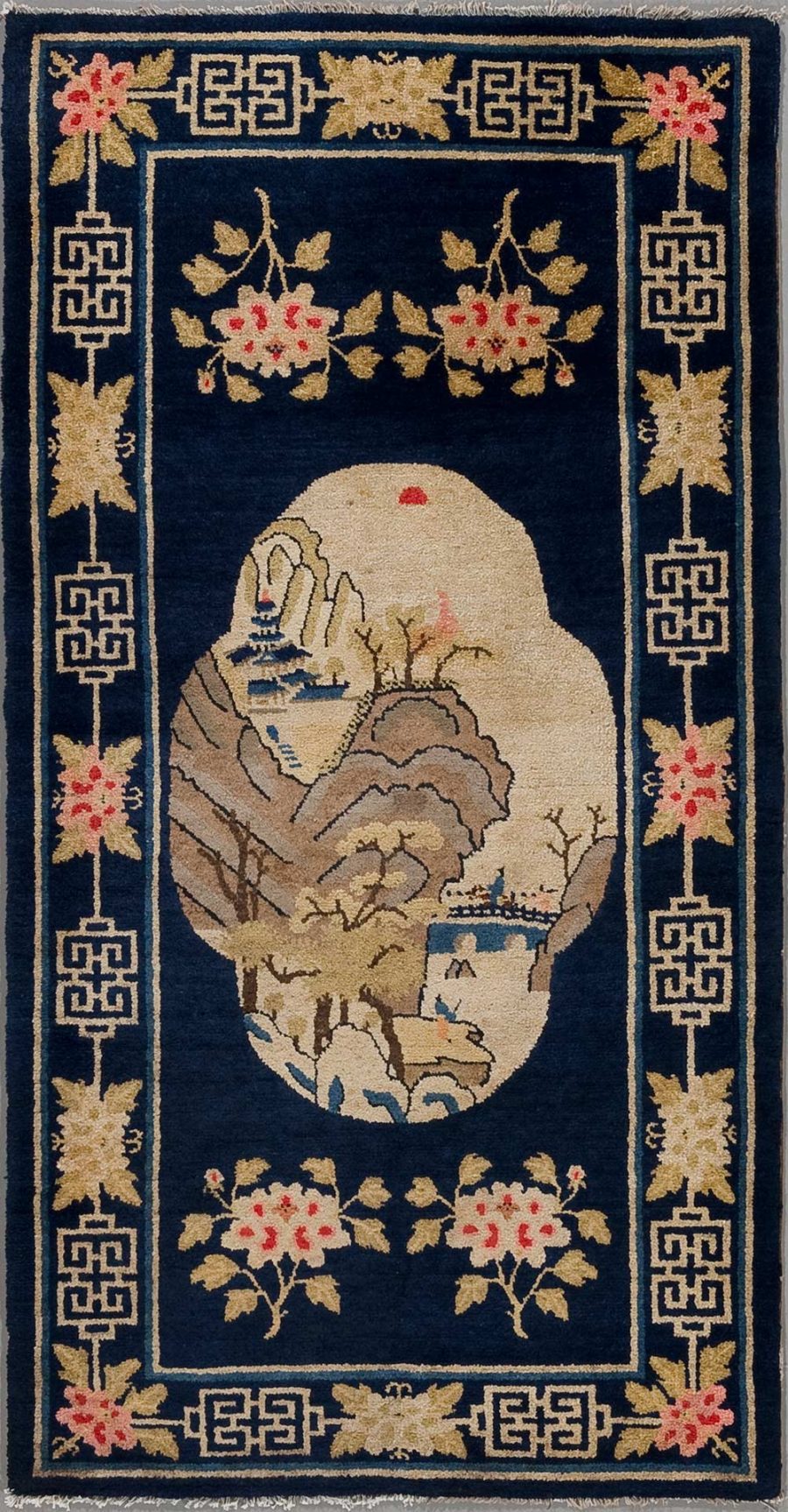 Traditioneller chinesischer Teppich mit aufwändigem floralem Muster und einer zentralen ovale Bildfläche, die eine Landschaftsszene mit Bergen, Bäumen, einem Gebäude und einem Boot auf Wasser zeigt. Der Teppich hat einen dunkelblauen Hintergrund mit beige- und rosafarbener Verzierung und geometrischen Motiven an den Rändern.