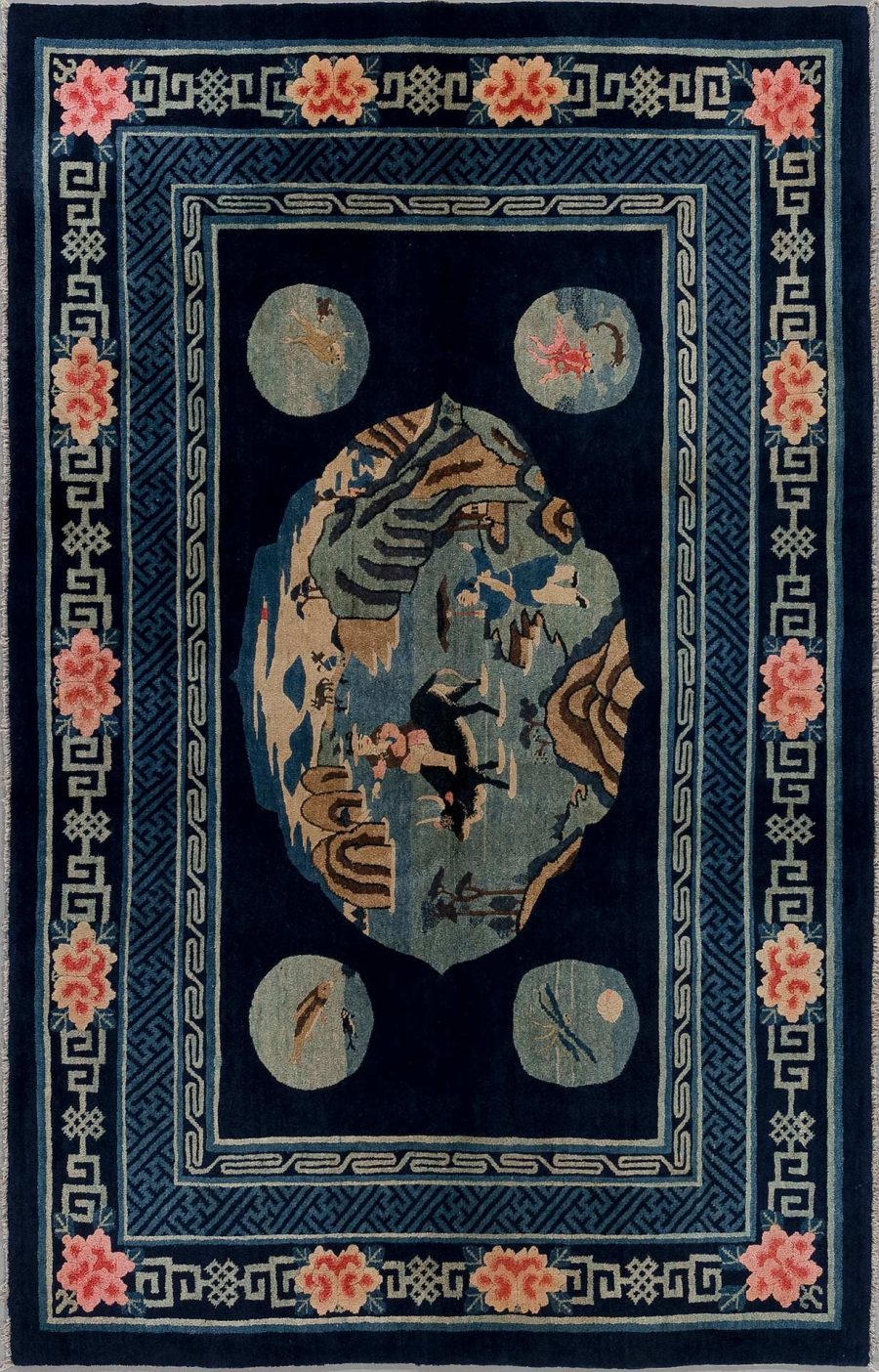 Antiker Teppich mit zentral ovaler Medaillonabbildung eines asiatisch inspirierten Berg- und Flusslandschaftsmotivs, umgeben von hellblauen und beige Ringformen auf dunkelblauem Grund mit blütenbesetzten Ecklösungen und griechischem Schlüsselband als Bordürendekor.