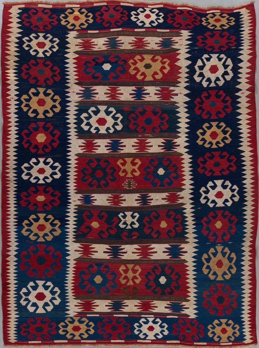 Traditioneller handgewebter Teppich mit geometrischen Mustern in Rot, Blau, Beige und Weiß.