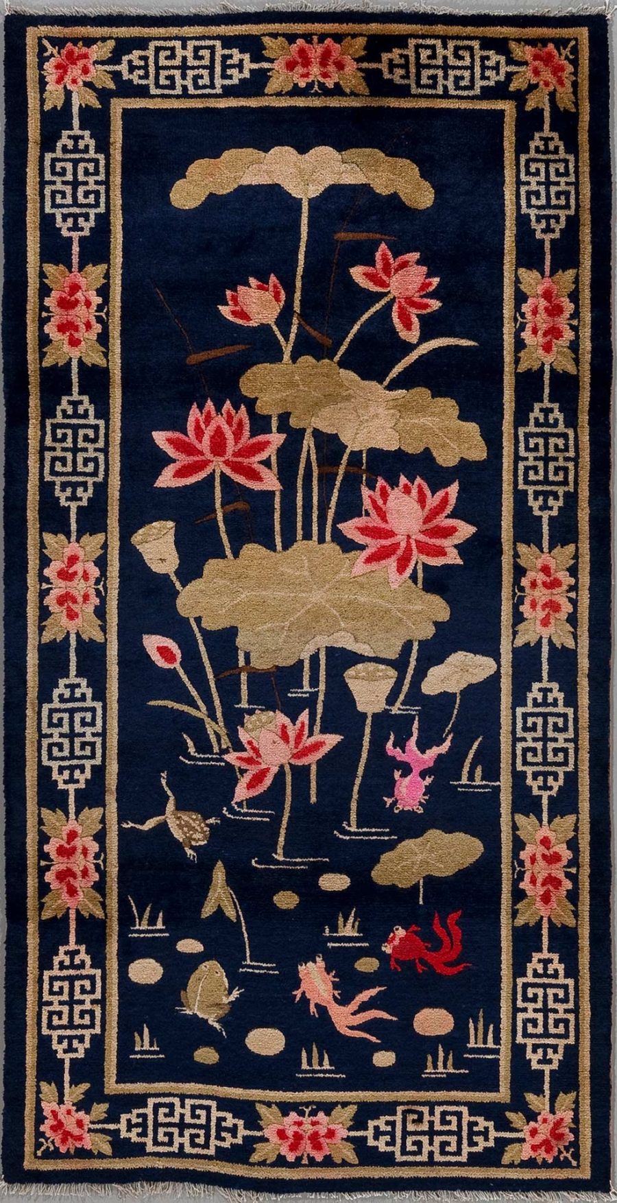Orientalischer Teppich mit dunkelblauem Hintergrund und asiatischen Motiven, darunter Lotusblüten in Rosa und Beige, Seerosenblätter, sowie stilisierte Karpfen und Frösche in Pink und Beige. Umrandet von einem beige-blauen Rand mit griechischen Schlüsselmotiven und floralen Elementen in den Ecken.