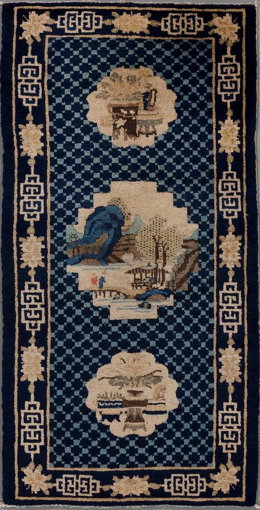 Traditioneller, vermutlich chinesischer Teppich aufrecht stehend, mit dunkelblauem Hintergrund und beigefarbenen Mustern, umfasst von geometrischem Randmuster. Zentrale Motive sind drei runde Medaillons mit asiatisch anmutenden Landschaftsszenen, darunter Bäume und Berge, sowie eine Figur auf einem der Medaillons.