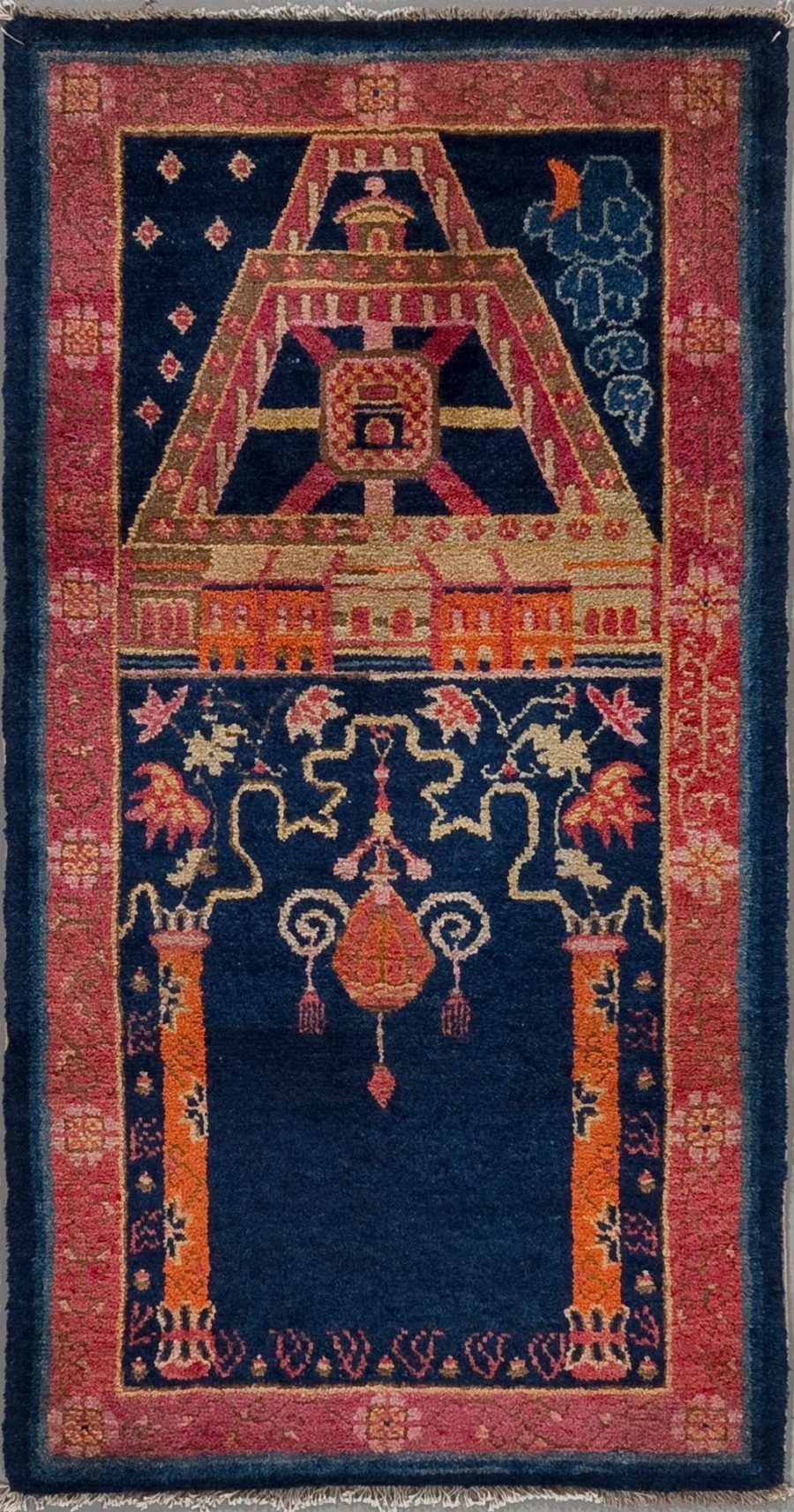Antiker handgeknüpfter Teppich mit einem persischen Tempelmuster, darstellend einen zentralen Kronleuchter, flankiert von Vasen und Blumenmotiven auf einem dunkelblauen Hintergrund und umrahmt von einem geometrisch gemusterten Rand in Pink, Orange und Cremetönen.