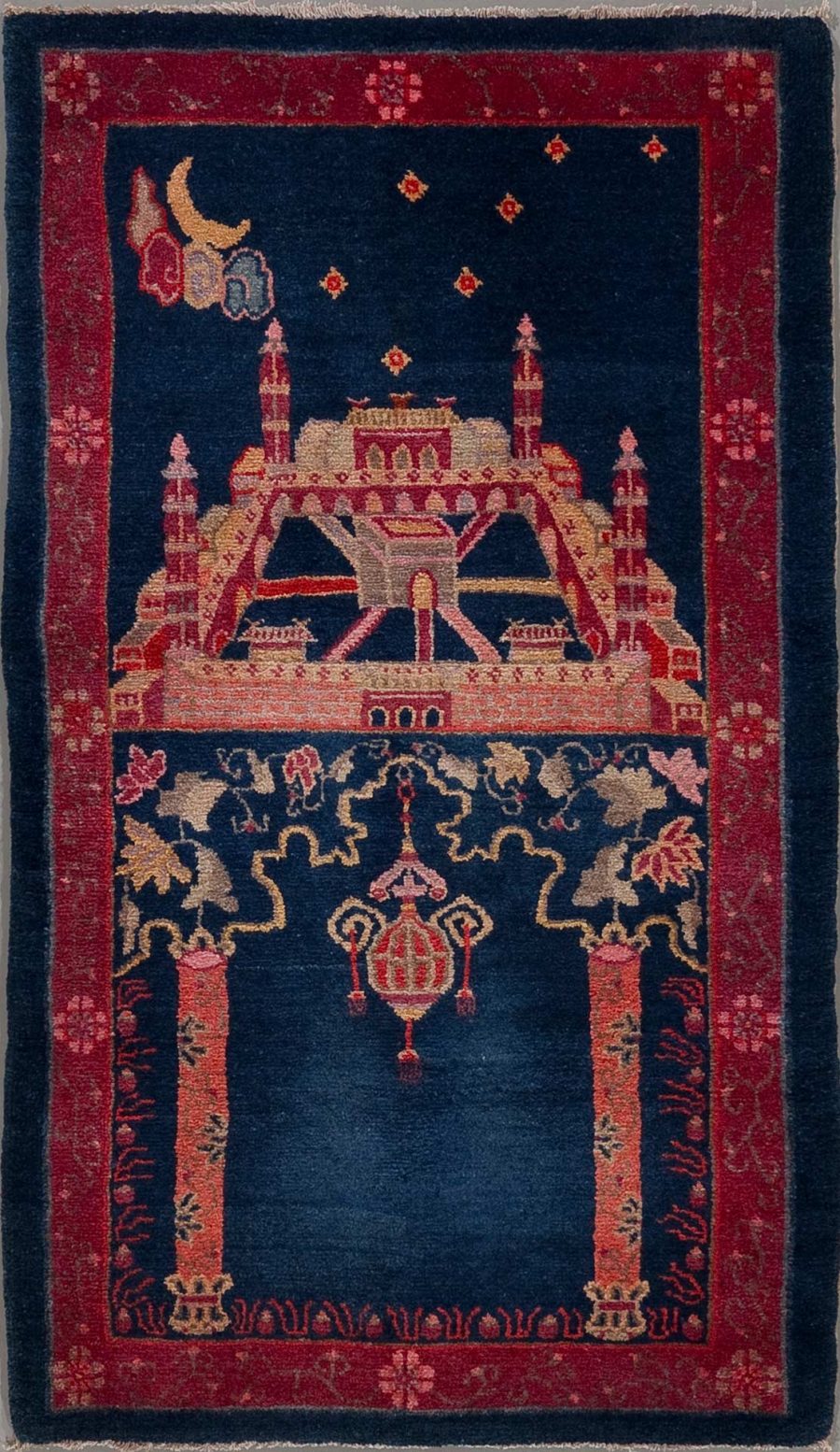 Traditioneller orientalischer Teppich mit detaillierter Darstellung einer Moschee oder eines Palastes in der Mitte, flankiert von Minaretten, umgeben von floralen Mustern und Bordüren; im oberen linken Bereich abgebildete Mondsichel und Sterne auf dunkelblauem Hintergrund.