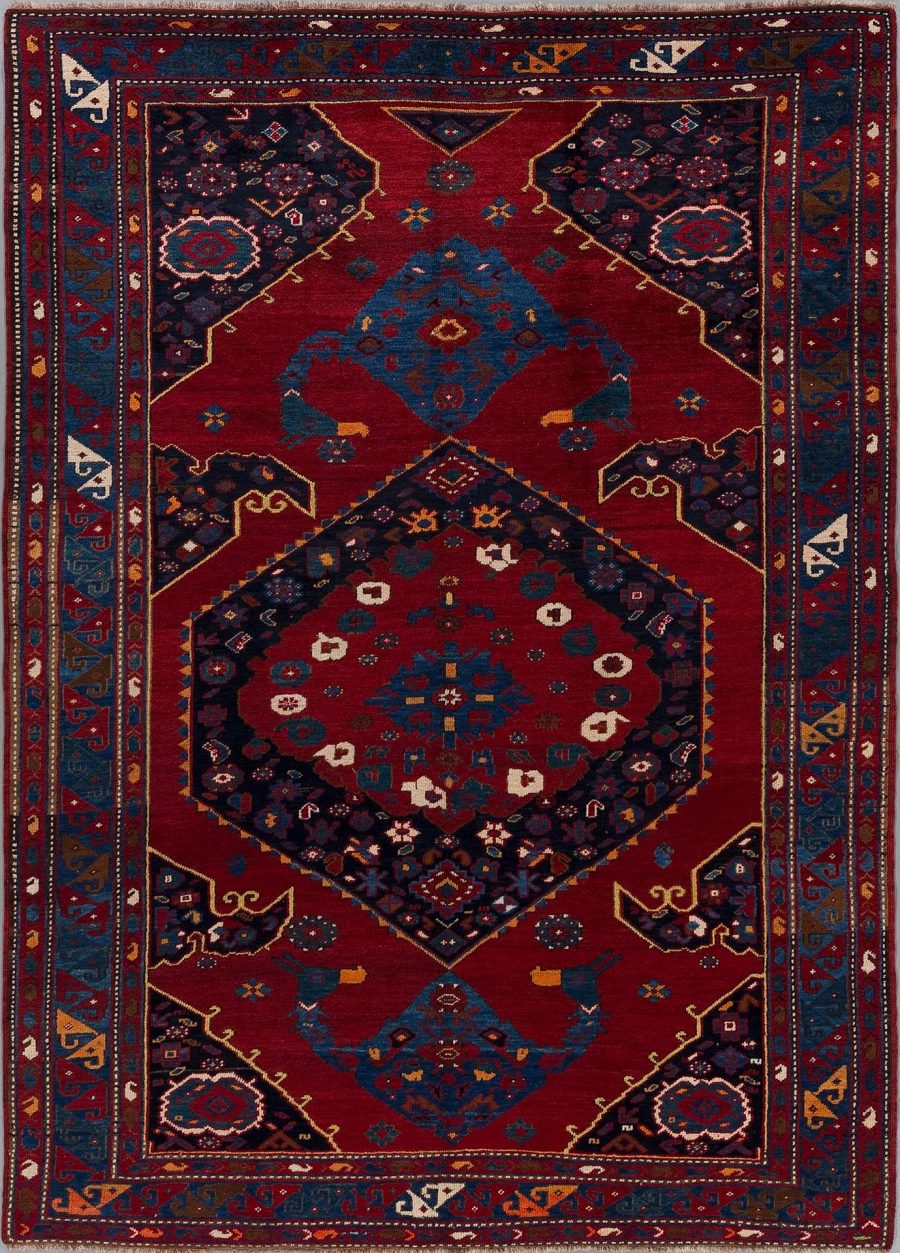 Traditioneller handgewebter Teppich mit komplexen Mustern in Rot, Blau, Beige und anderen Akzentfarben, mit zentraler Diamantform und umlaufenden Bordüren.