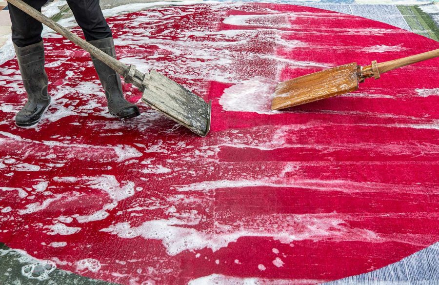 Person reinigt einen roten Teppich mit Schaum und zwei großen Bürsten.