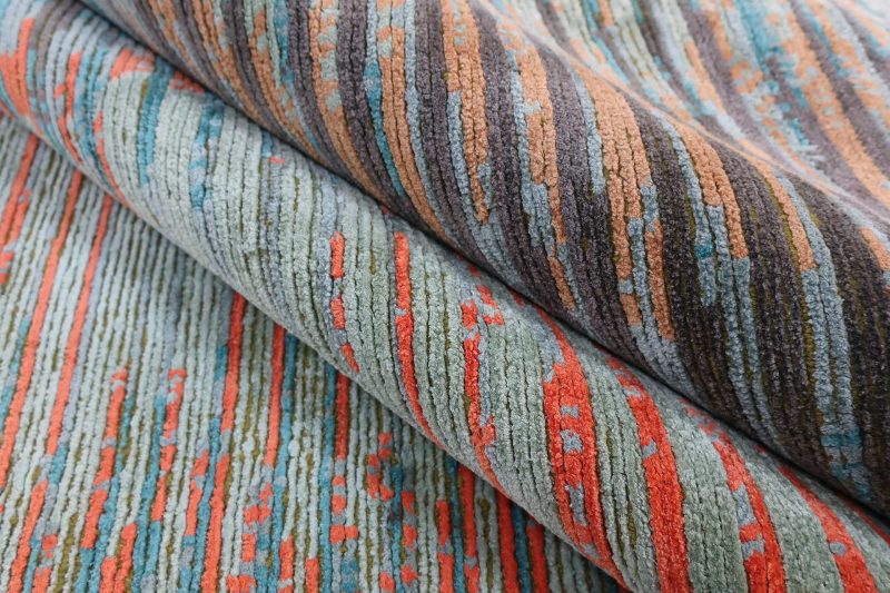 Nahaufnahme eines zusammengerollten Teppichs mit bunten, gemusterten Streifen in verschiedenen Schattierungen von Grün, Orange, Grau und Blau.