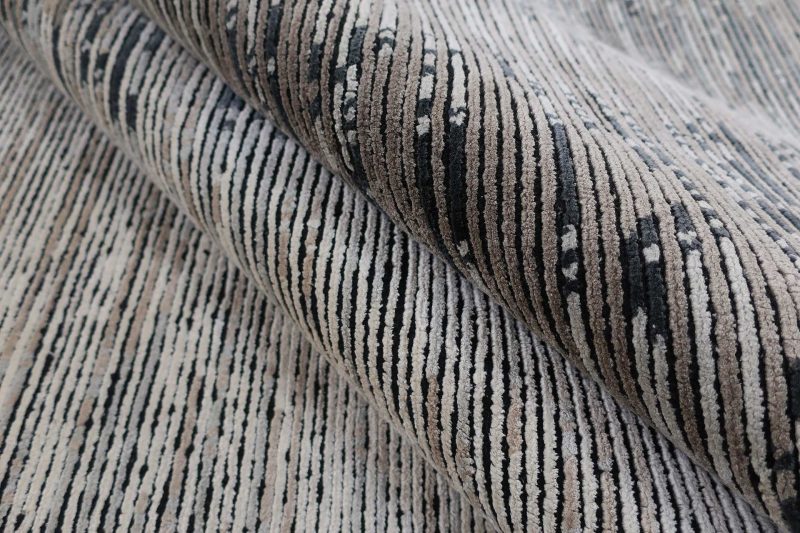 Nahaufnahme eines zusammengerollten Teppichs mit einem Streifenmuster in Schwarz, Grau und Beige.