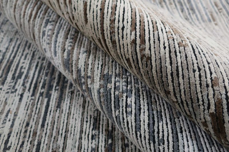 Nahaufnahme eines zusammengerollten Teppichs mit gestreiftem, texturiertem Muster in Grau-, Beige- und Brauntönen.
