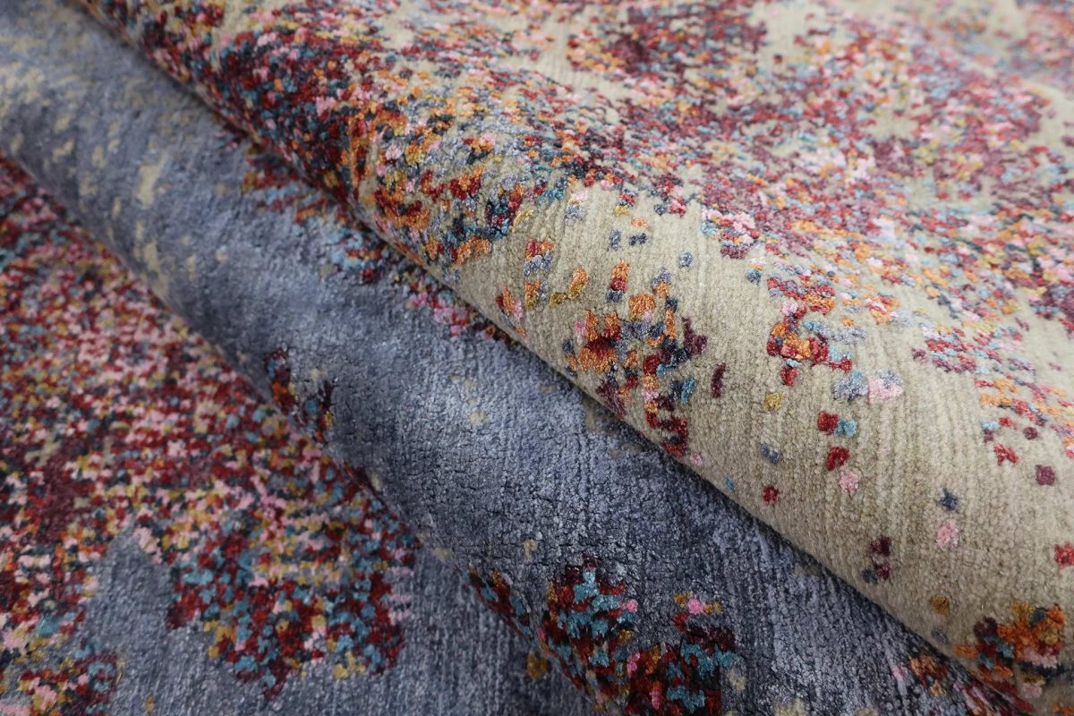 Nahaufnahme eines Teppichs mit farbenfrohen Fleckenmustern auf beigem und grauem Grund.