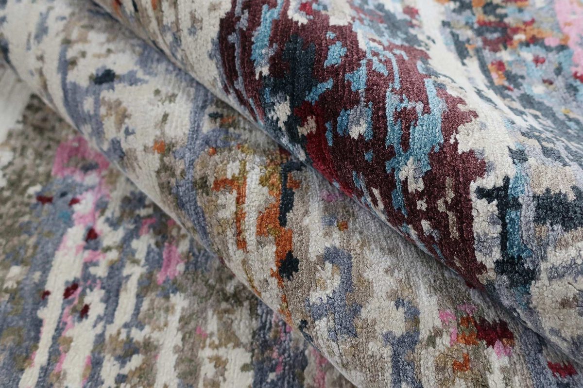 Nahaufnahme verschiedener gemusterter Teppiche, die übereinanderliegen, mit sichtbaren Mustern und Farbabstufungen in Rot, Blau, Beige und anderen Farbtönen.