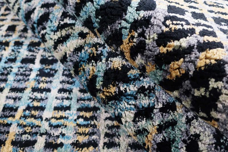 Nahaufnahme eines texturierten Teppichs mit abstraktem Muster in Schwarz, Blau, Grau und Gelbtönen.