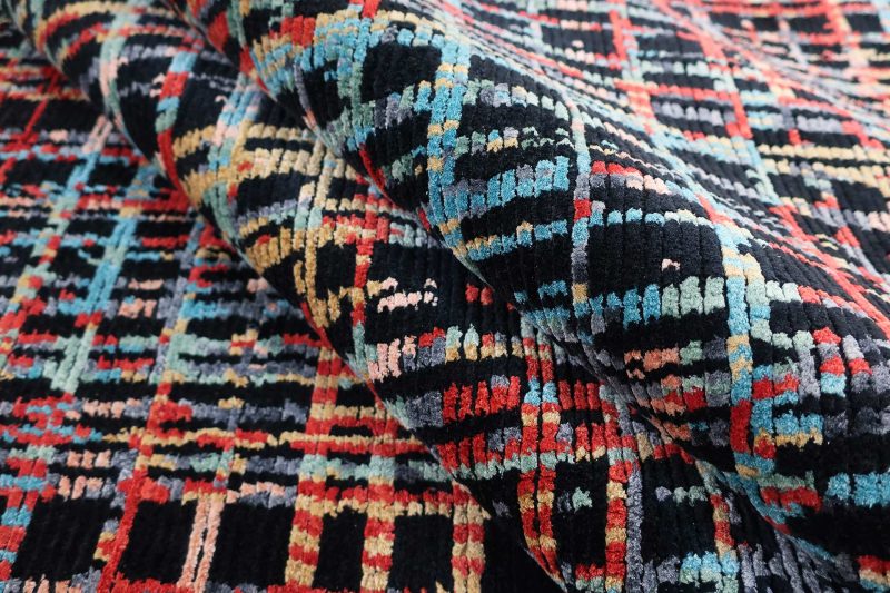 Nahaufnahme eines bunten, gemusterten Teppichs mit unregelmäßigen geometrischen Formen in den Farben Schwarz, Rot, Blau, Grün und Gelb.